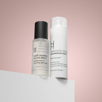Two bottles—Magnesium Spray and Pillow Mist—stand side by side on a white surface with a pink background, ideal for rest and relaxation.