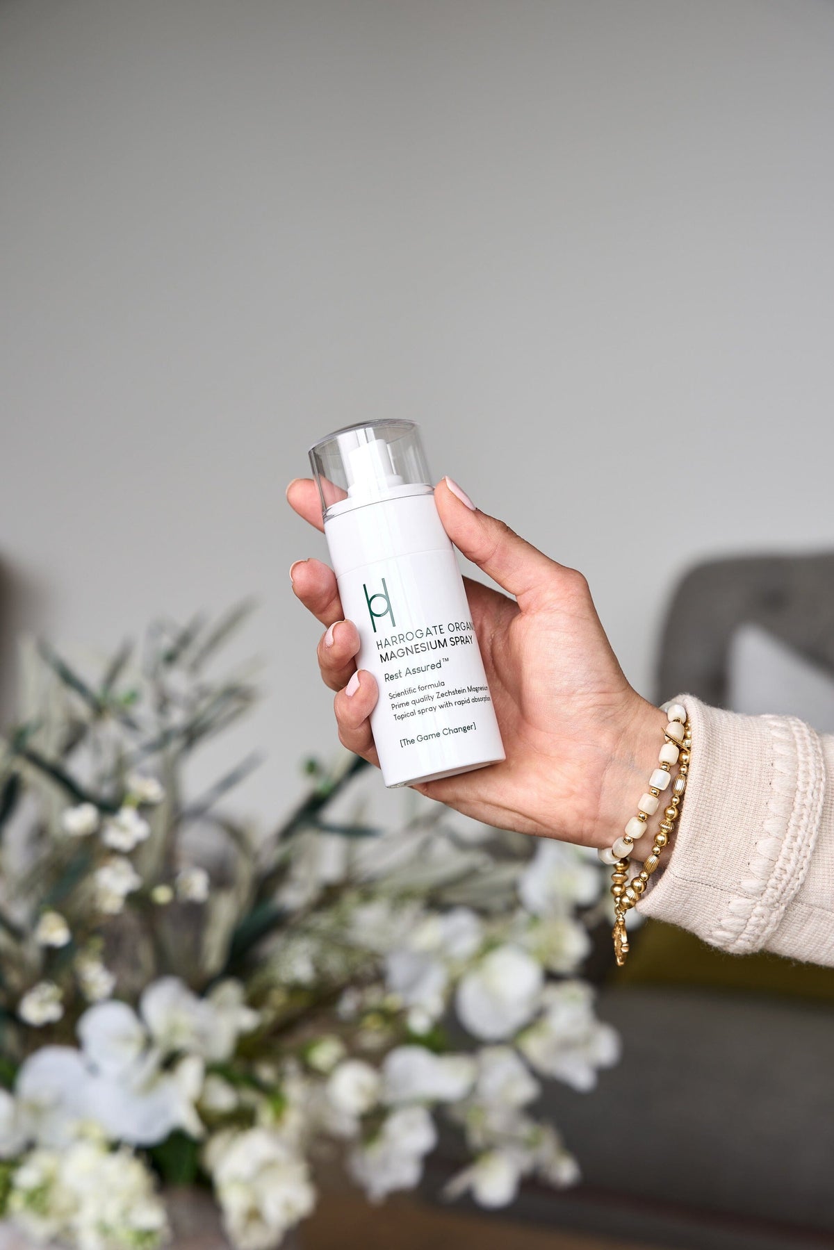 Hand holding Harrogate Organics Magnesium Spray with flowers in the background