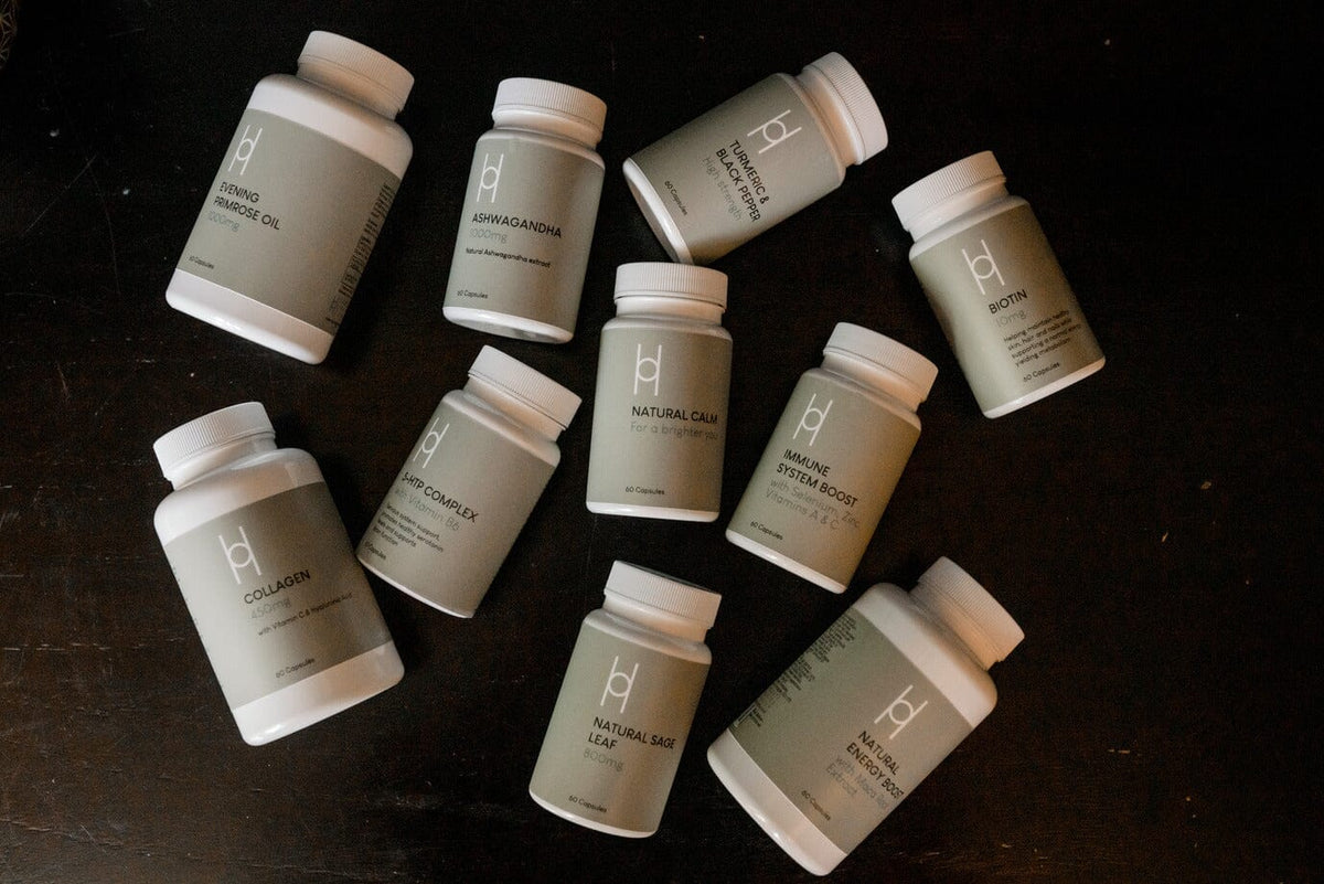 An overhead shot of a collection of assorted supplement bottles with light grey labels and white caps arranged on a dark wooden surface.