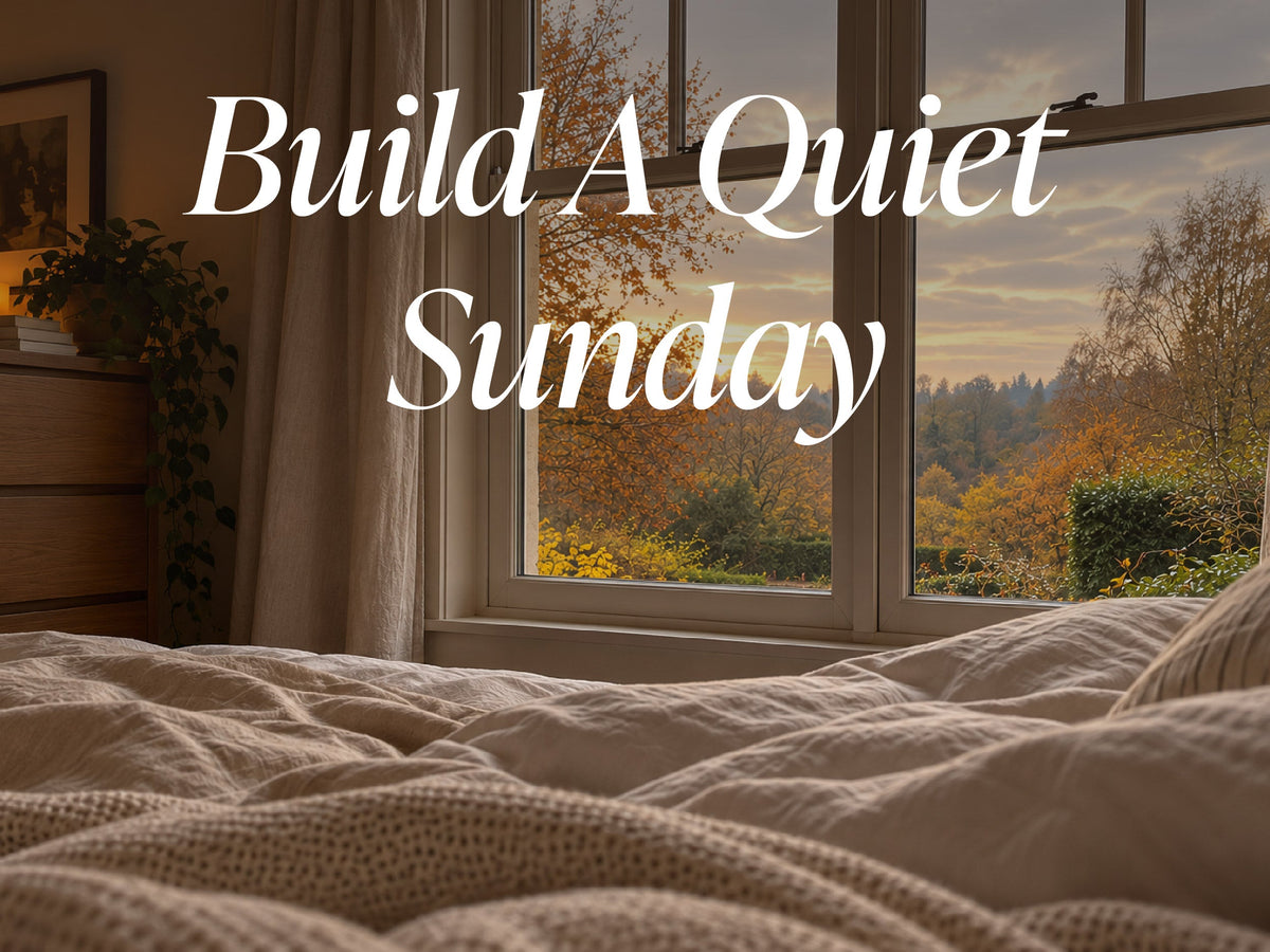 Text reading Build A Quiet Sunday overlaid on an image of a bed looking out a window at an autumn landscape.