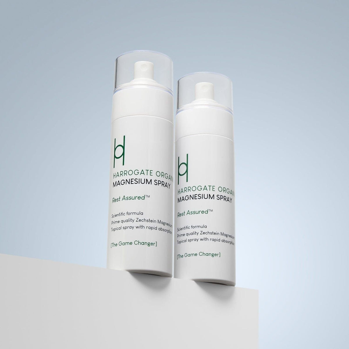 Two white bottles of Harrogate Organics Magnesium Spray Duo Bundle (2 x 150ml) with clear caps stand on a white surface against a light blue background. The calming natural sleep aid features green and black text on the labels.