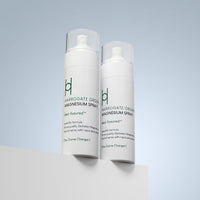 Two white bottles of Harrogate Organics Magnesium Spray Duo Bundle (2 x 150ml) with clear caps stand on a white surface against a light blue background. The calming natural sleep aid features green and black text on the labels.