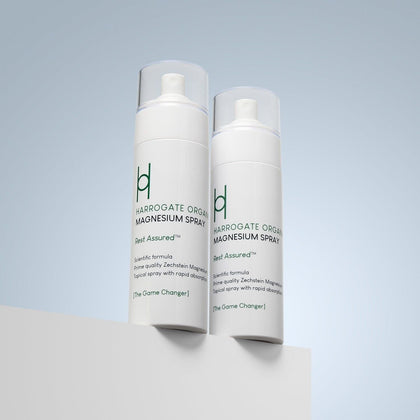 Two white bottles of Harrogate Organics Magnesium Spray Duo Bundle (2 x 150ml) with clear caps stand on a white surface against a light blue background. The calming natural sleep aid features green and black text on the labels.