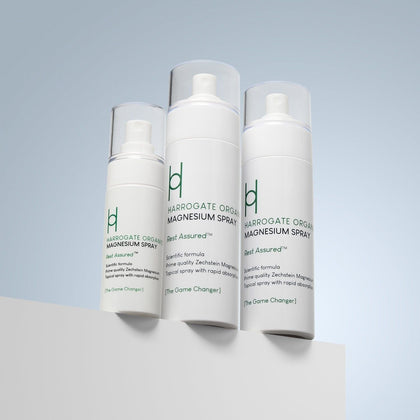 Three white bottles of Harrogate Organics Magnesium Spray - Travel Pack, featuring green text and clear caps, are displayed on a white surface against a light blue gradient background and arranged from smallest to largest.