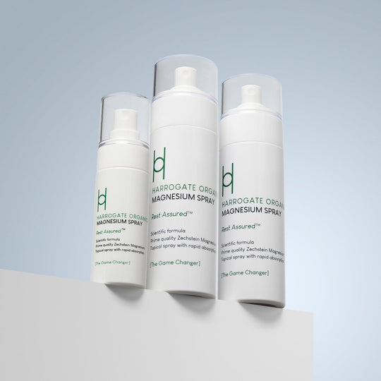 Three white bottles of Harrogate Organics Magnesium Spray - Travel Pack, featuring green text and clear caps, are displayed on a white surface against a light blue gradient background and arranged from smallest to largest.