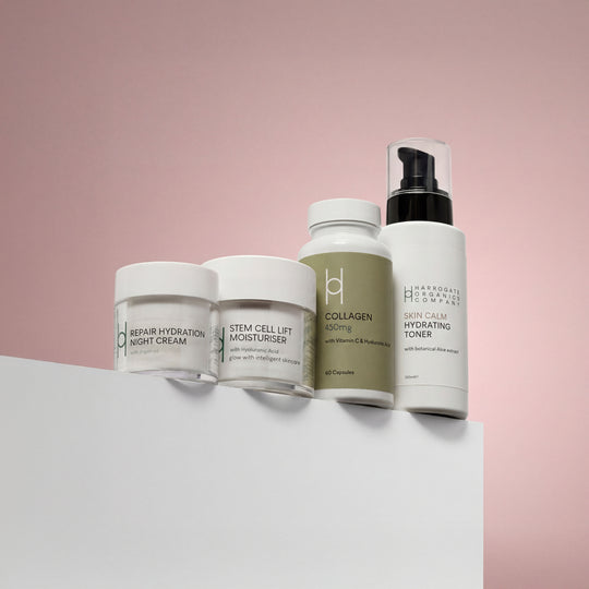 The Day & Night Skin Repair Bundle, featuring night cream, stem cell moisturiser, collagen nutrition capsules, and hydrating toner in minimalist white containers, is arranged on a white surface with a pink background.