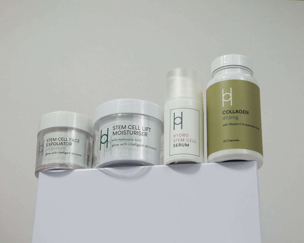 The Age Defying Set, featuring a face exfoliator, lift moisturizer, hydro stem cell serum, and collagen supplement capsules, is neatly arranged on a white surface with a plain background for youthful-looking skin.