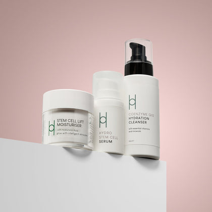 The Anti-Ageing Skincare Routine | 3-Step Daily Skincare Set features three white containers displayed on a white surface against a pink background—ideal for your daily anti-aging regimen.