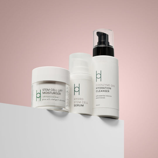 The Anti-Ageing Skincare Routine | 3-Step Daily Skincare Set features three white containers displayed on a white surface against a pink background—ideal for your daily anti-aging regimen.