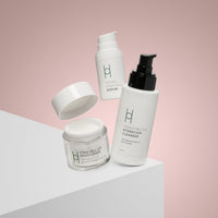 The Anti-Ageing Skincare Routine | 3-Step Daily Skincare Set, in sleek white minimalist packaging, is displayed on a white surface with a soft pink background, showcasing its modern and appealing design.