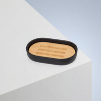 A Sustainable Sugar Cane Soap Dish with a wooden insert rests on the corner of a white geometric surface against a light blue background.