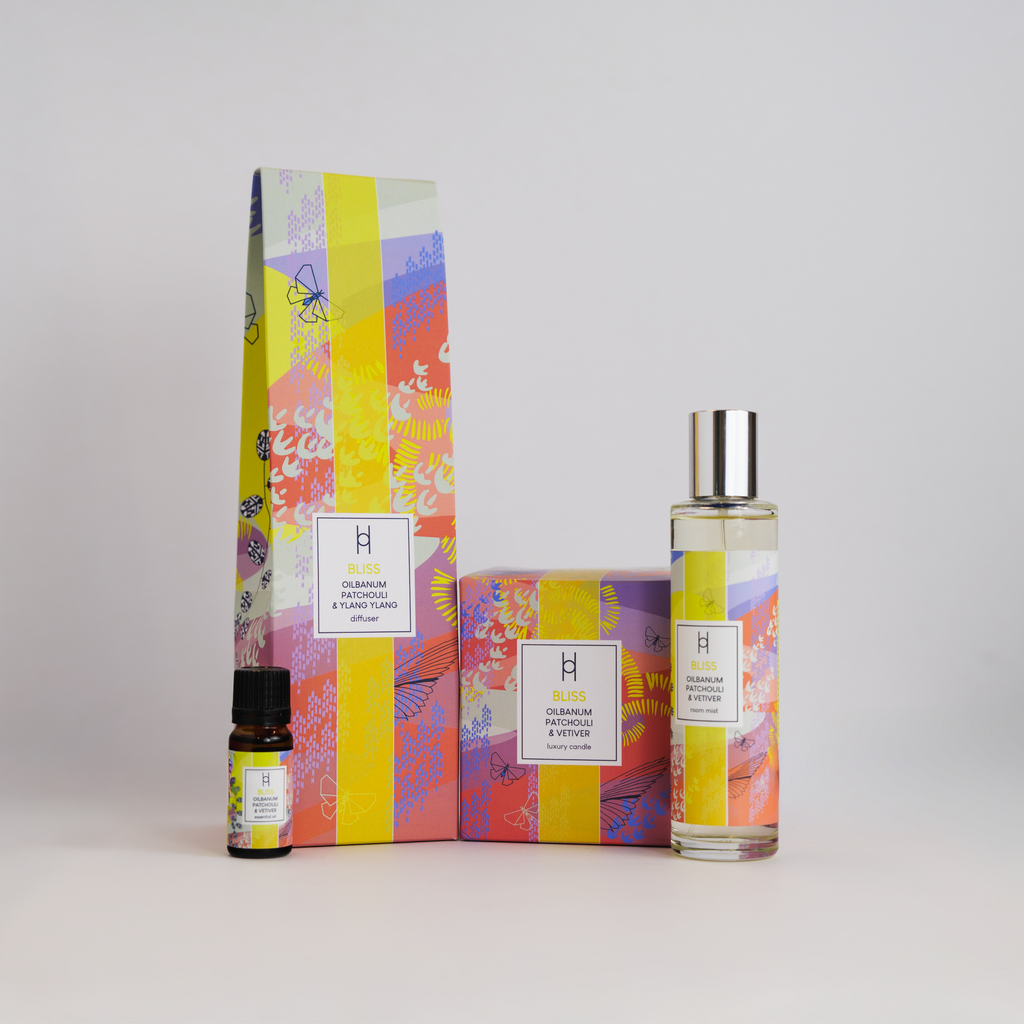 Three "Deluxe Home Collection - Bliss" perfumes with colorful, patterned packaging sit on a white background: a small dropper bottle, a medium box, and a tall spray bottle with matching box—ideal for home fragrance.