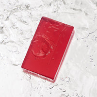 The Calm Chamomile - Luxe Chamomile Soap, a rectangular red translucent vegan bar with bubbles on its surface, rests on a reflective watery background with scattered droplets.