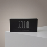 A black rectangular box labeled "Luxury Candle Care Kit" with outlined images of a candle snuffer and wick cutter sits on a white surface against a neutral background.