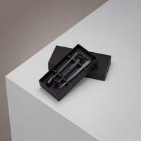The Luxury Candle Care Kit, in a black box with lid slightly open, features three sleek black grooming tools—including a wick cutter and tweezers—displayed on a white and gray geometric surface.