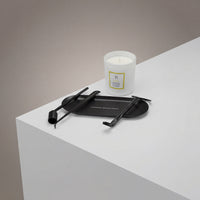 The Luxury Candle Care Kit, featuring a wick cutter and two accessories, is displayed beside a white jar candle on a white surface with a black tray, set against a neutral gray background.