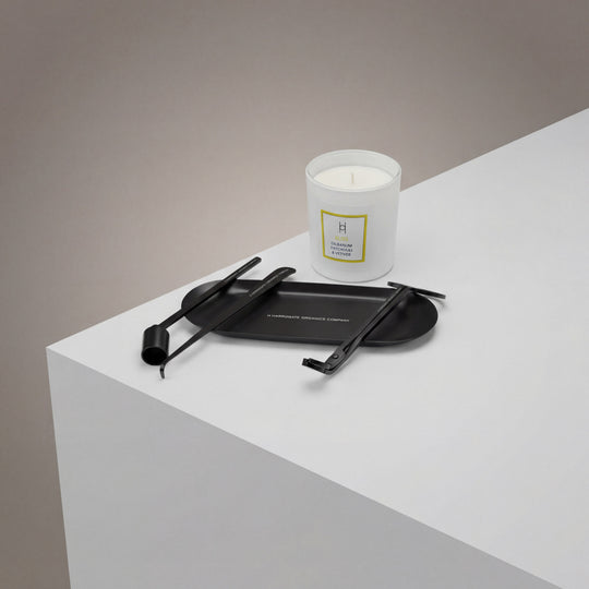 The Luxury Candle Care Kit, featuring a wick cutter and two accessories, is displayed beside a white jar candle on a white surface with a black tray, set against a neutral gray background.
