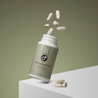 An open bottle of Daily Essentials: Multivitamins for Men 50+ lies tilted on a greenish background, with several tablets—formulated for immune support—spilling out and resting on a white surface beside it.