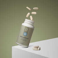 A bottle of Daily Wellness: Multivitamins for Men Under 50 lies on its side with beige tablets spilling out, displayed on a white surface against a muted green background.