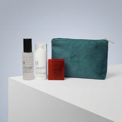 The Deep Sleep Gift Set features a teal zippered pouch embossed with "Sleep. Deep. Sleep." and includes a calming trio: a spray bottle, pump bottle, and small red soap bar—all displayed on a white geometric surface with a light blue backdrop.