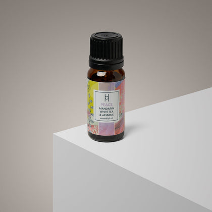 A 10ml amber glass bottle labeled "Peace Essential Oil Blend | Mandarin & Jasmine" rests on a minimalist white surface with a neutral beige background, emphasizing the calming, vegan-friendly aroma.