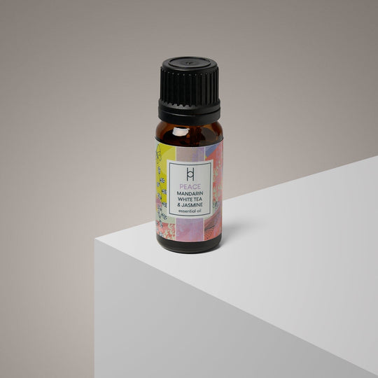 A 10ml amber glass bottle labeled "Peace Essential Oil Blend | Mandarin & Jasmine" rests on a minimalist white surface with a neutral beige background, emphasizing the calming, vegan-friendly aroma.