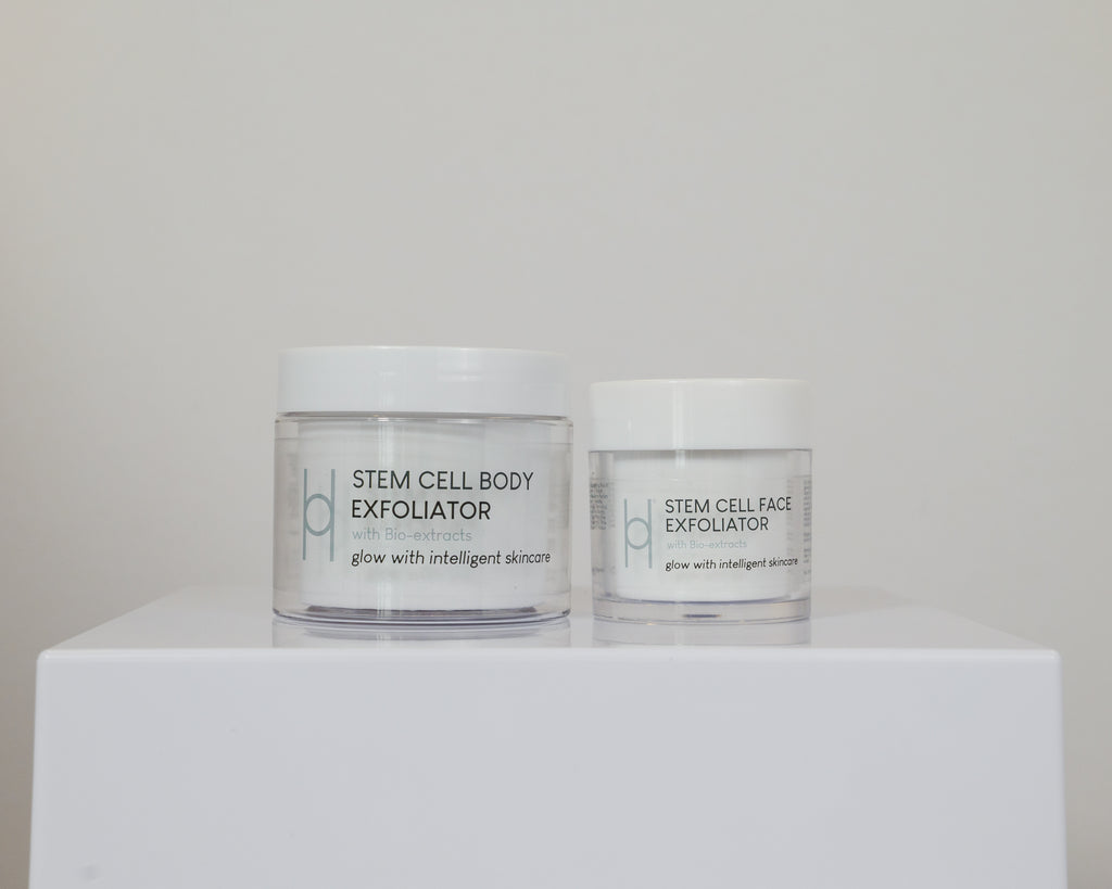 The Exfoliator Duo, featuring two white jars for face and body with bio-lux extracts to reveal radiant skin, is displayed on a white surface against a plain background.
