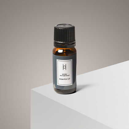 A 10ml amber bottle of Winter Wonderland Essential Oil—Citrus Orange & Cedar—rests on a white surface against a gray background. Its luxury minimalist label and black cap evoke an inviting winter scent.