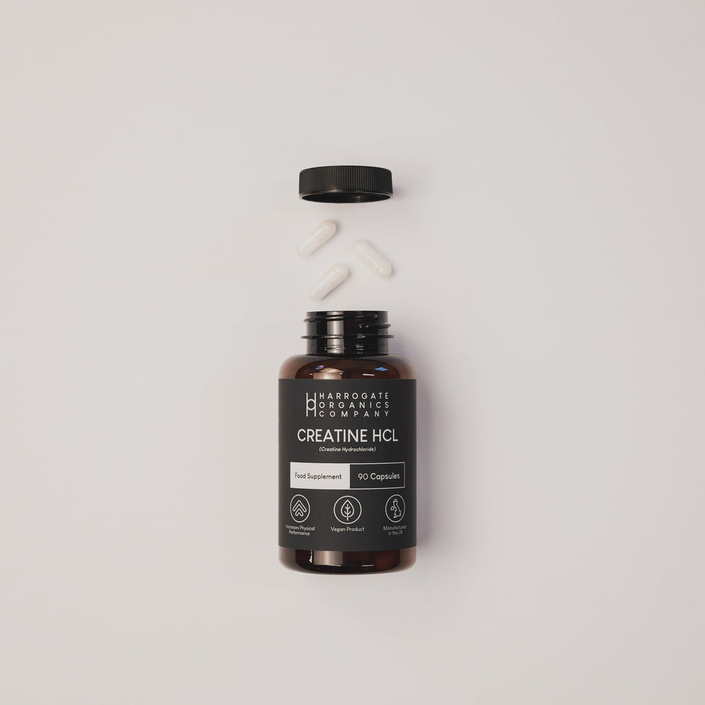 A brown bottle of Creatine HCL Supplement (30 Day Supply, 90 x 750mg capsules) sits on a white surface with its black cap off and four white capsules above, highlighting convenient dosing for muscle growth and rapid absorption.