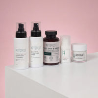 Five products from the Hair, Skin & Nails Complex and Skincare Bundle by Harrogate Organics are displayed in a row on a white surface with a pink background—including cleanser, toner, capsules, serum, and moisturizer—all expertly crafted to deliver enriching nutrients for comprehensive 360-degree skincare.