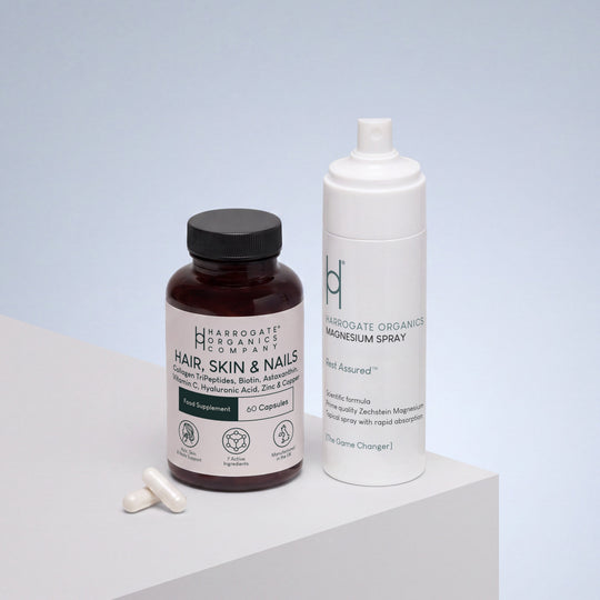The Hair, Skin & Nails Complex and 150ml Magnesium Spray Bundle is displayed on a white surface against a blue gradient background, featuring the capsule bottle with two white capsules beside it and the tall magnesium spray—perfect for daily self-care and muscle wellness.