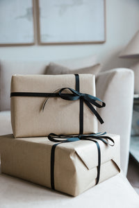 Gift Wrap in brown paper with black ribbon bows enhances the look of a beige sofa, creating a special touch against a neutral room with blurred framed artwork in the background.
