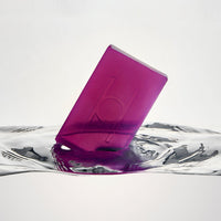 The Lavender Fields - Luxe Soap, a translucent purple rectangular vegan bar, stands at an angle in clear water, creating ripples on the surface.