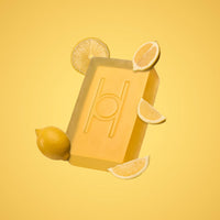 Lemon Grove - Luxe Soap: a yellow, moisturising bar with a circular and vertical line design, displayed among whole and sliced lemons on a solid yellow background.