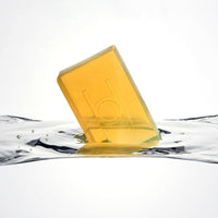 The Lemon Grove - Luxe Soap is a translucent yellow bar with a simple embossed design, floating upright in clear water against a white background.