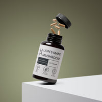 A dark bottle labeled Lion's Mane Mushroom Supplement 800mg Per Serving - 30 Day Supply - 60 Capsules spills capsules on a plain olive background. The vegan, non-GMO, gluten-free extract supports brain function.