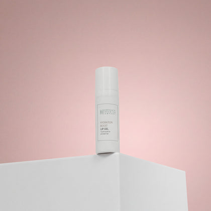 A white bottle labeled Hydration Boost Lip Gel | Fuller, Hydrated Lips | 10ml stands upright on a white surface with a soft pink gradient backdrop.