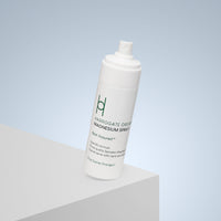 A white spray bottle labeled Harrogate Organics Magnesium Spray - 150ml sits on a light gray surface against a gradient blue background. Minimalist green and black text highlights its natural, soothing sleep aid benefits and convenient spray nozzle.