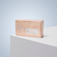 A rectangular bar of Fresh Mandarin - Luxe Soap, wrapped in peach paper with a koi fish design, sits on a white geometric surface. The label highlights clean, nourished skin. The background is light blue.