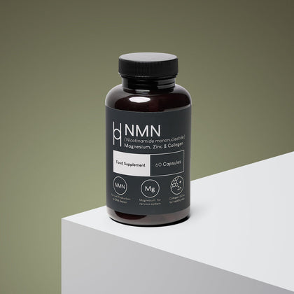 A brown bottle labeled "NMN, Magnesium, Zinc & Collagen Supplement 700mg NMN Per Serving - 30 Day Supply - 60 Capsules" sits on a white surface with a green gradient background, highlighting its wellness-support formula.