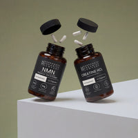 The NMN & Creatine HCL Supplement Bundle features two brown bottles with black caps and capsules above, set on a white geometric surface against a green background—ideal daily supplements for your foundation.