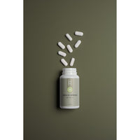 A white bottle of Natural Defence with Vitamin C sits on a green surface, its lid off and several white capsules scattered nearby.