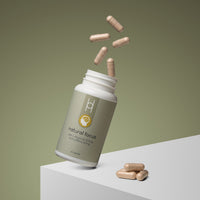 A bottle of Natural Focus with L-Theanine 100mg and Caffeine 50mg spills beige capsules, some midair and others on a white surface, set against a plain olive-green background—emphasizing its focus-boosting blend.