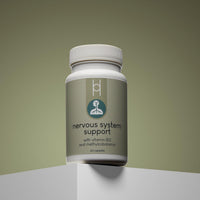 A bottle of Nervous System Support with Vitamin B12 and Methylcobalamin sits on a white platform against a muted green background. It contains 60 capsules for daily nervous system support.
