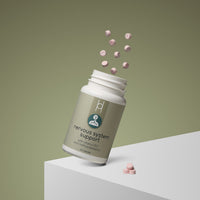 A white bottle labeled "Nervous System Support with Vitamin B12 and Methylcobalamin" displays pink tablets on and above a white surface, set against a muted green background. Some tablets rest on the surface while others float in mid-air.