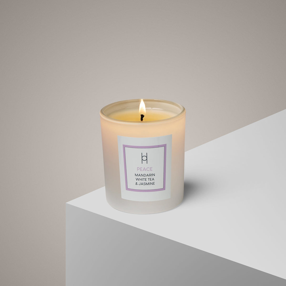 The Peace Aromatherapy Candle | Mandarin, White Tea & Jasmine | Hand-Poured adds calm with its soothing scent in a frosted glass holder on a white surface, set against a soft gray background.