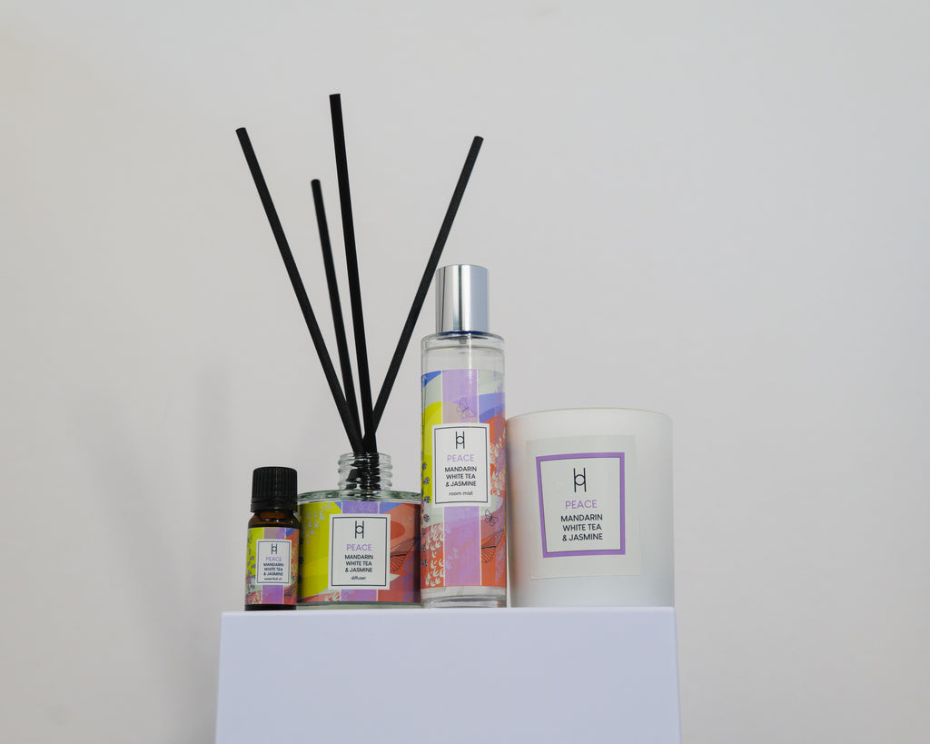 The Deluxe Home Collection - Peace features a reed diffuser, essential oil, spray, and white candle in Mandarina, White Tea & Jasmine scents, all displayed together on a white pedestal against a plain background.