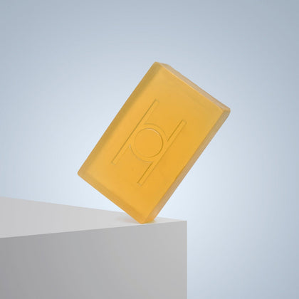 The Pure Goodness Soap - Unscented, a translucent yellow vegan bar with an embossed circular design, stands upright on a white edge against a light blue background.