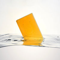 Pure Goodness Soap - Unscented: A translucent amber vegan bar with a debossed logo stands upright in clear water against a white background—ideal for sensitive skin.