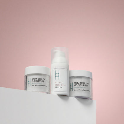 The Radiant Skin Gift Set | Glow-Boosting Skincare Collection features three white-packaged products—a Face Exfoliator, Serum, and Stem Cell Lift Moisturiser—displayed on a white surface against a soft pink background.